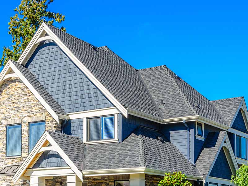 Higher end, mid-class home with a gray shingle roof, as well as blue vinyl and stone siding
