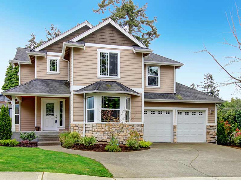 Exterior view of a mid-class, two-story home with beige vinyl siding and stone siding towards the bottom