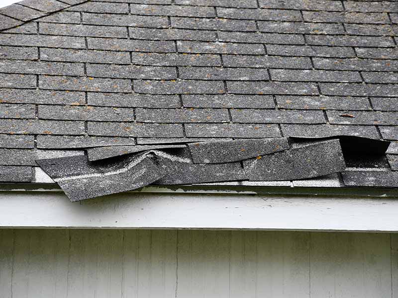 Close up of a residential roof with shingles about to fall off due to a storm